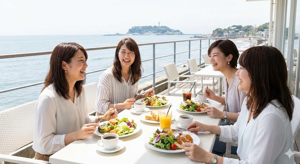 葉山の海を一望できるお洒落なカフェのテラス席で、ランチと会話を楽しむ女性グループの様子。